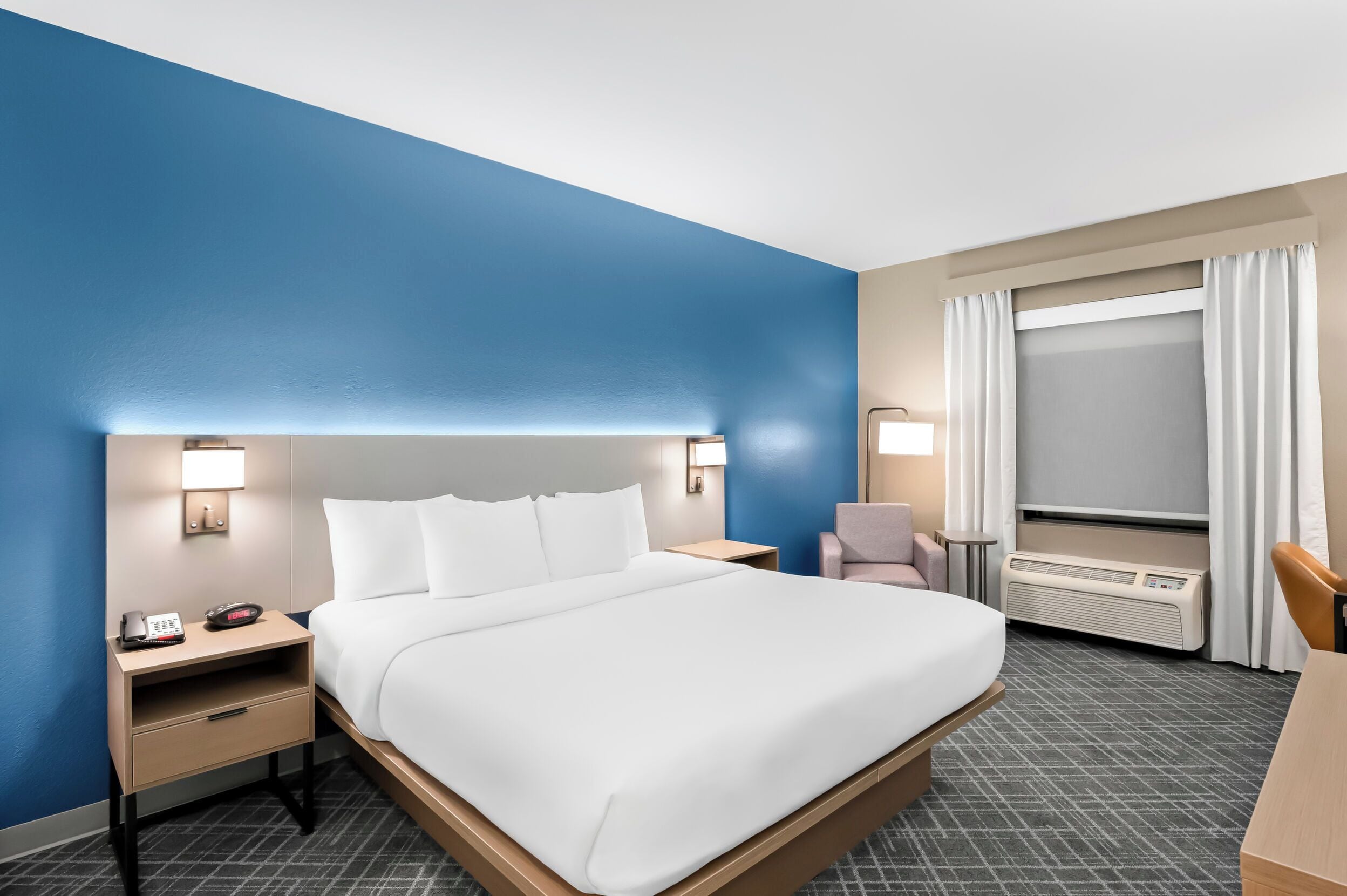 Quarto de hotel com uma cama grande, mesas de cabeceira, uma escrivaninha e uma janela com cortinas.