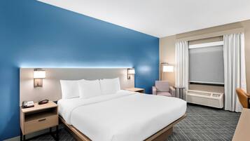 Quarto de hotel com uma cama grande, mesas de cabeceira, uma escrivaninha e uma janela com cortinas.