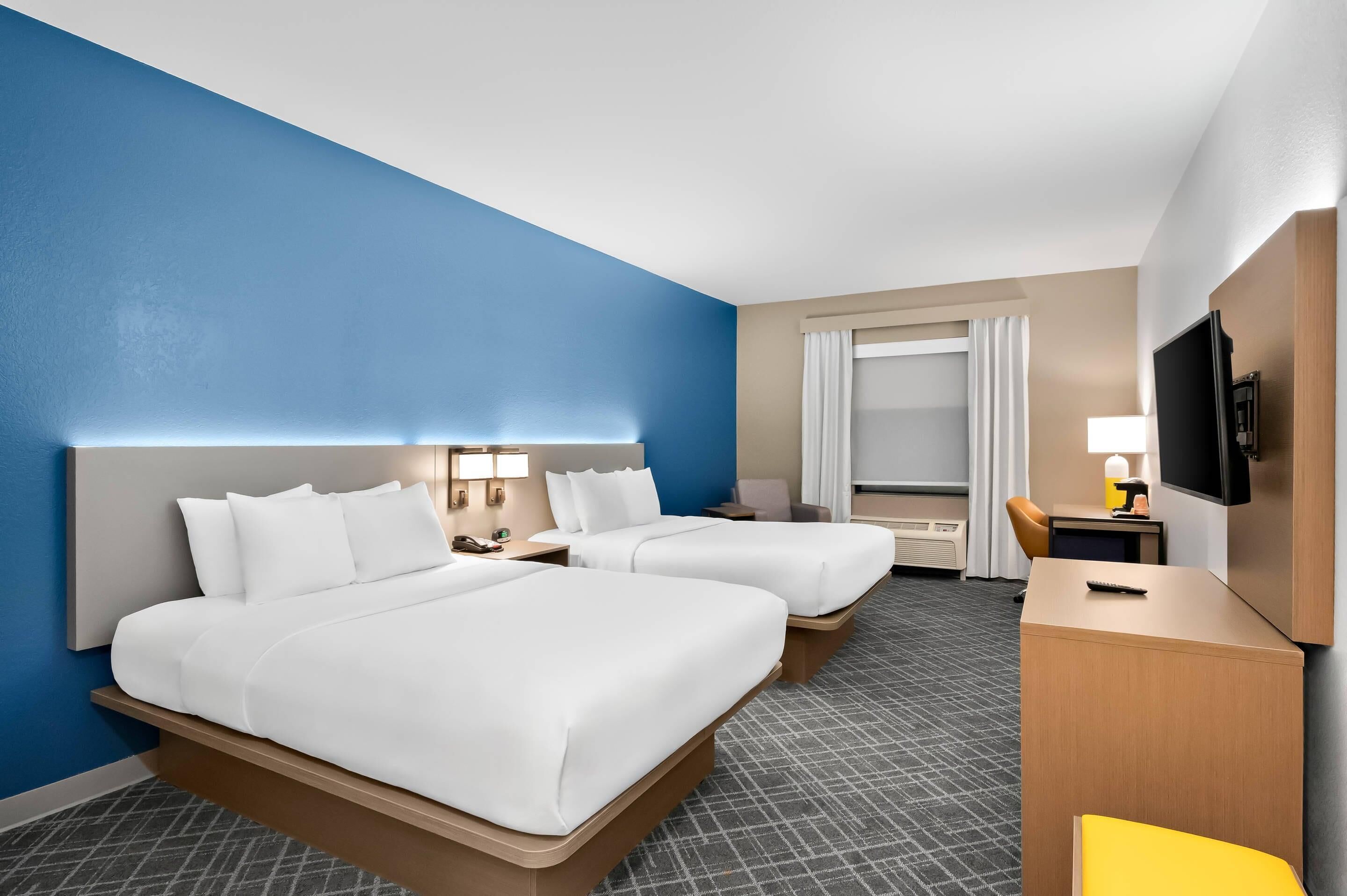 Ein Hotelzimmer mit zwei Betten, einem Schreibtisch, einem Fernseher und einem fenster mit Vorhängen.
