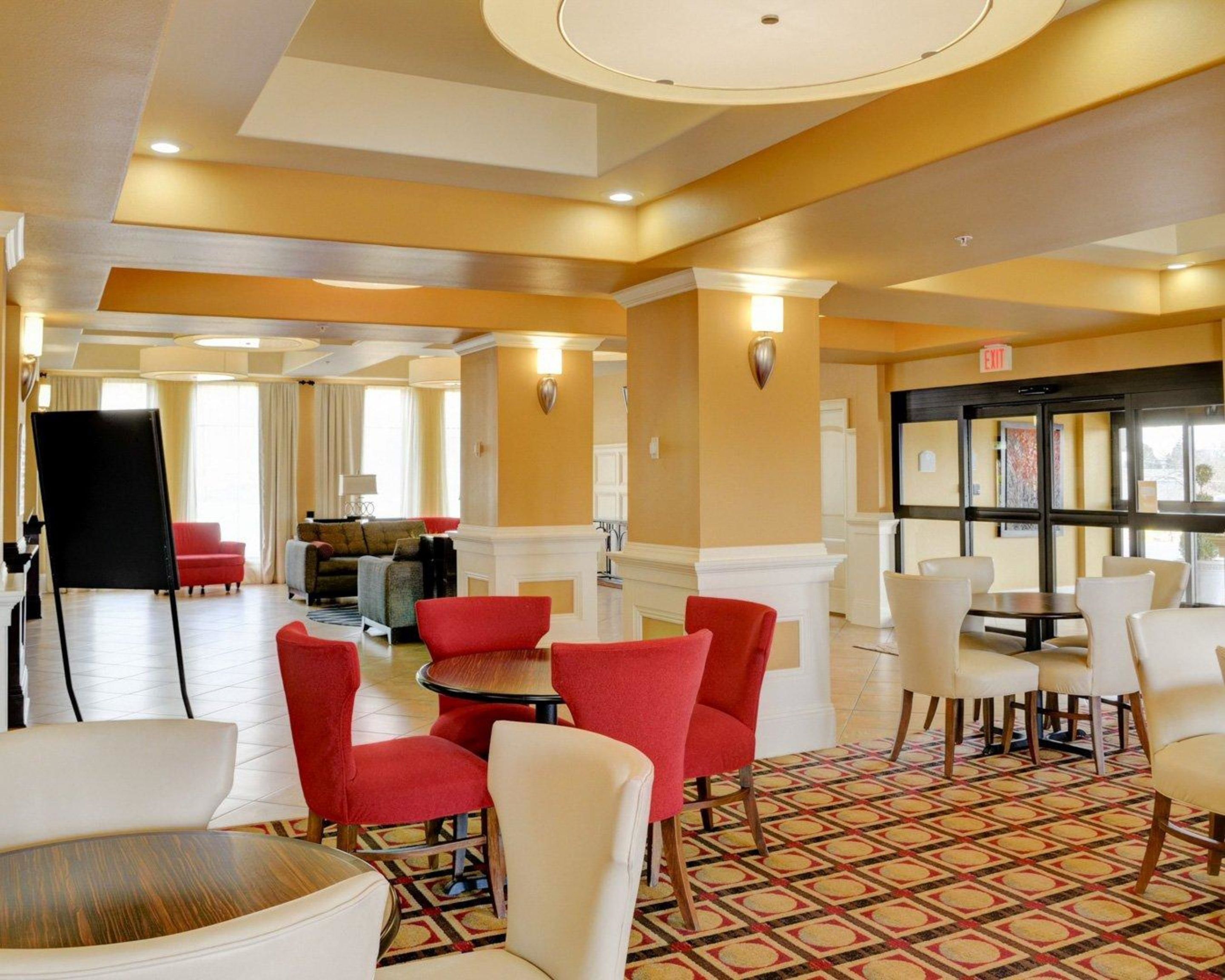 A spacious hotel lobby with a mix of red and white chairs, a black easel, and a patterned carpet.