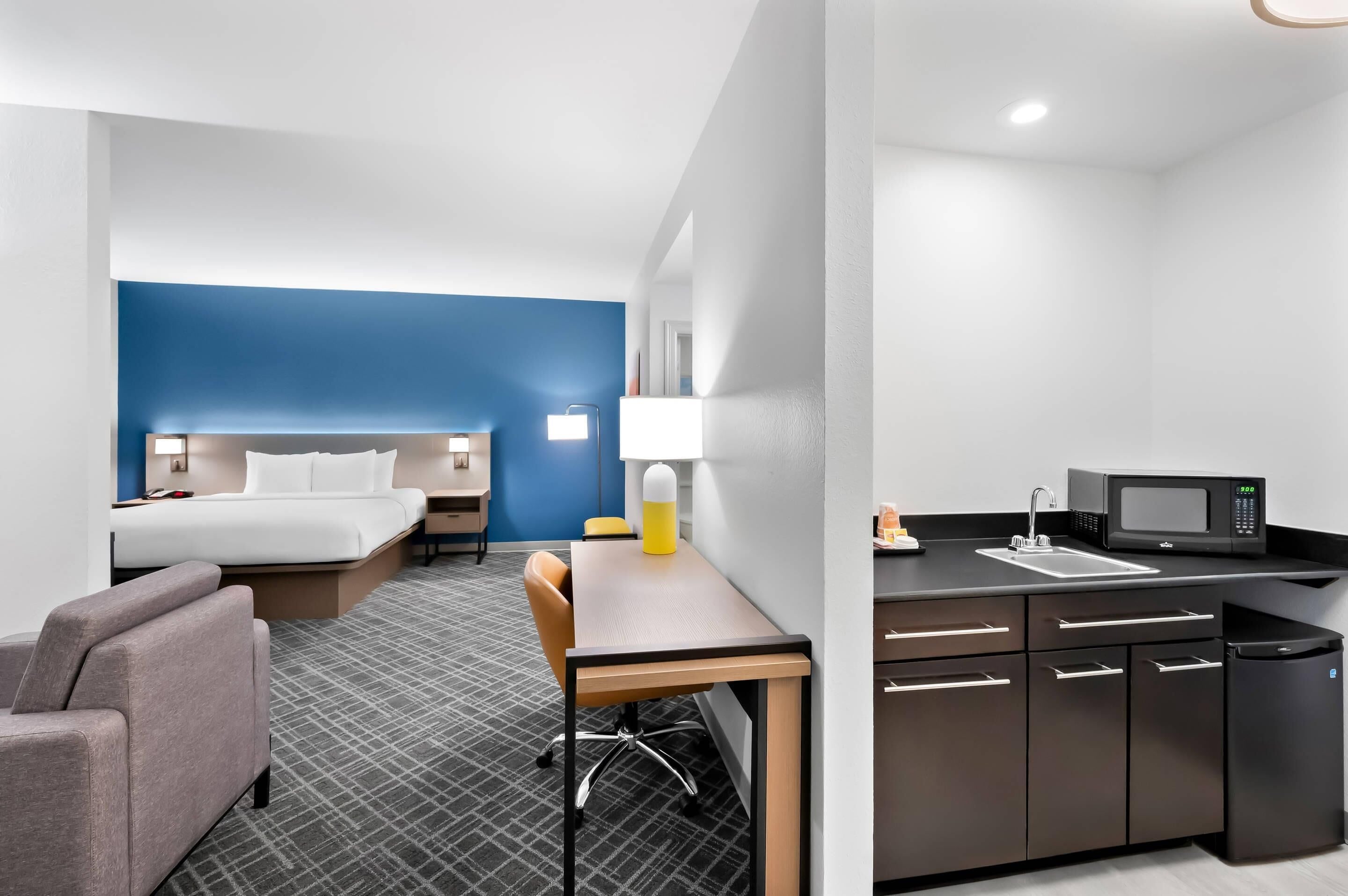 A hotel room with a bed, bedside table, lamp, and a small desk with a chair.