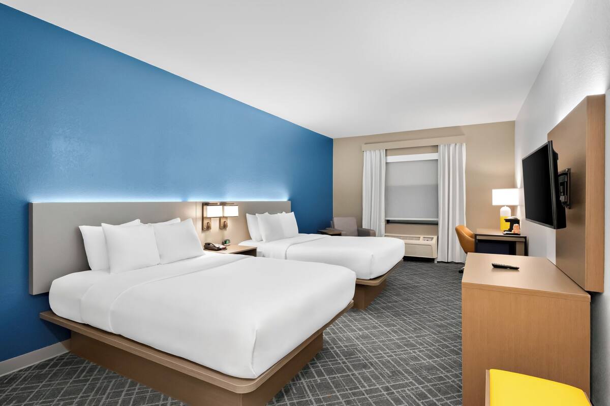 A hotel room with two beds, a desk, a TV, and a window with curtains.