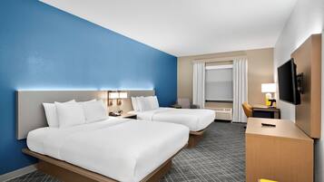 A hotel room with two beds, a desk, a TV, and a window with curtains.