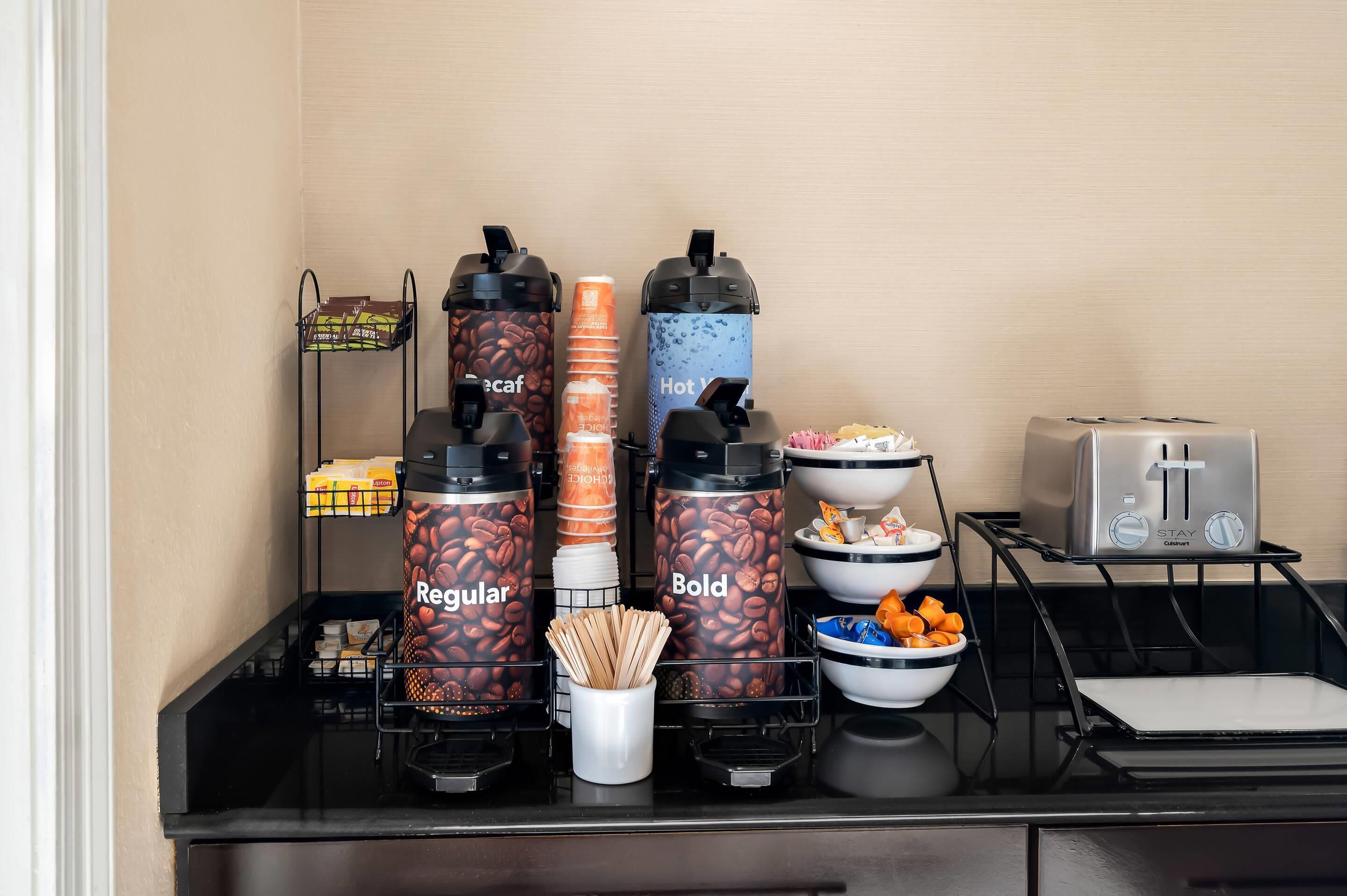 A self-service coffee station with branded dispensers, a toaster, and various coffee pods.