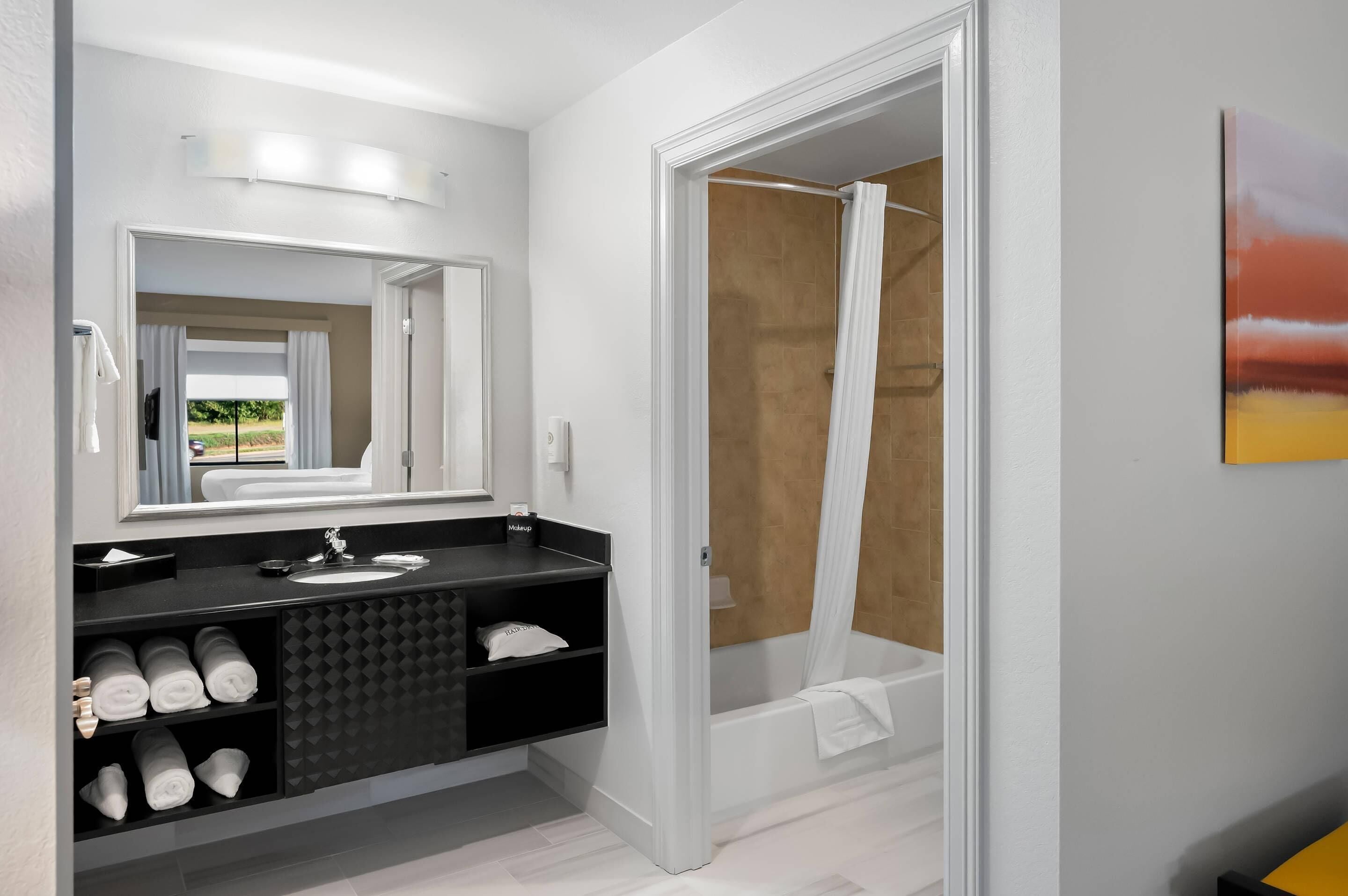 A modern bathroom with a large mirror, a black vanity, a white sink, and a shower area.