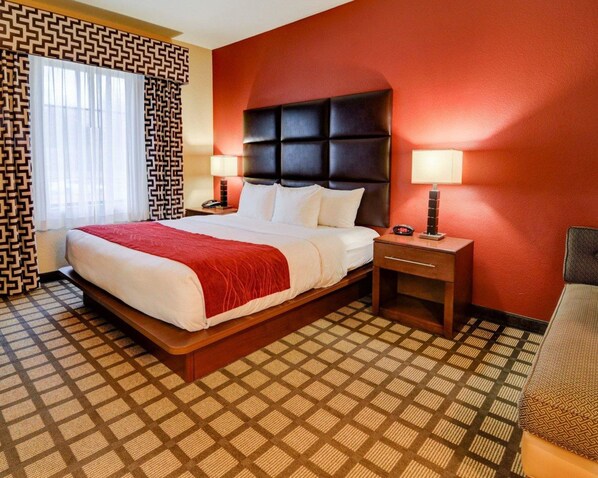 A hotel room with a large bed, a nightstand with a lamp, and a patterned carpet.