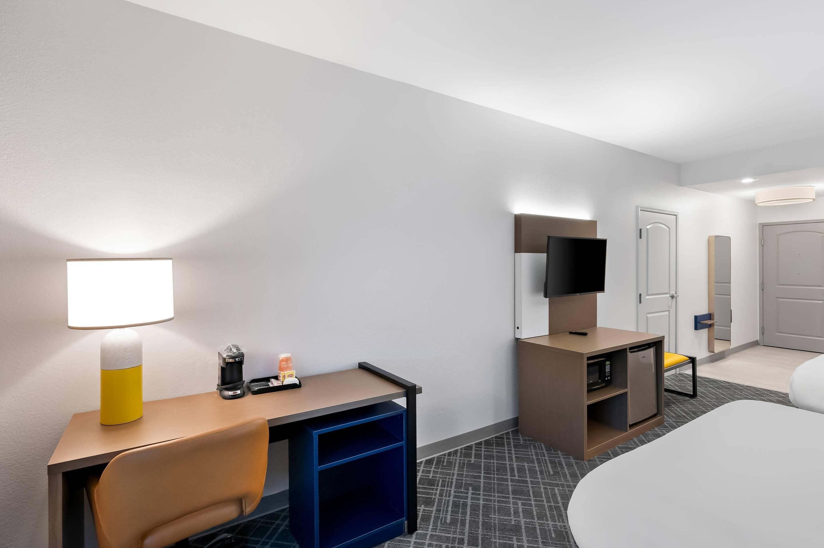Habitación de hotel con escritorio, silla, cama, televisión y un mueble pequeño.