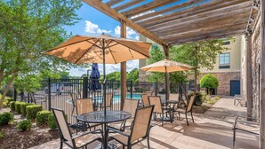 An outdoor patio area with tables and chairs under pergolas, a pool in the background, and a stone building facade. - Comfort Inn & Suites Fort Smith I-540 (Fort Smith)