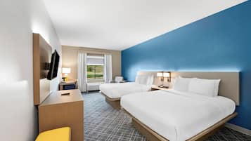 A hotel room with two beds, a desk, a chair, a TV, and a window with a view of greenery.