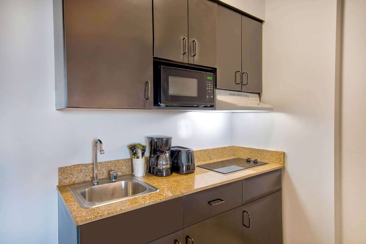 A compact kitchen with a stainless steel sink, a microwave, a coffee maker, and a toaster on a granite countertop.