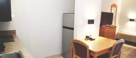 A compact kitchen with a refrigerator, a sink, a wooden dining table with two chairs, and a mirror above the dresser.