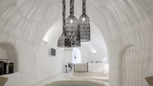 A modern, white interior with a central hot tub, black hanging pendant lights, and a minimalist design. - Aroma Suites (Santorini)