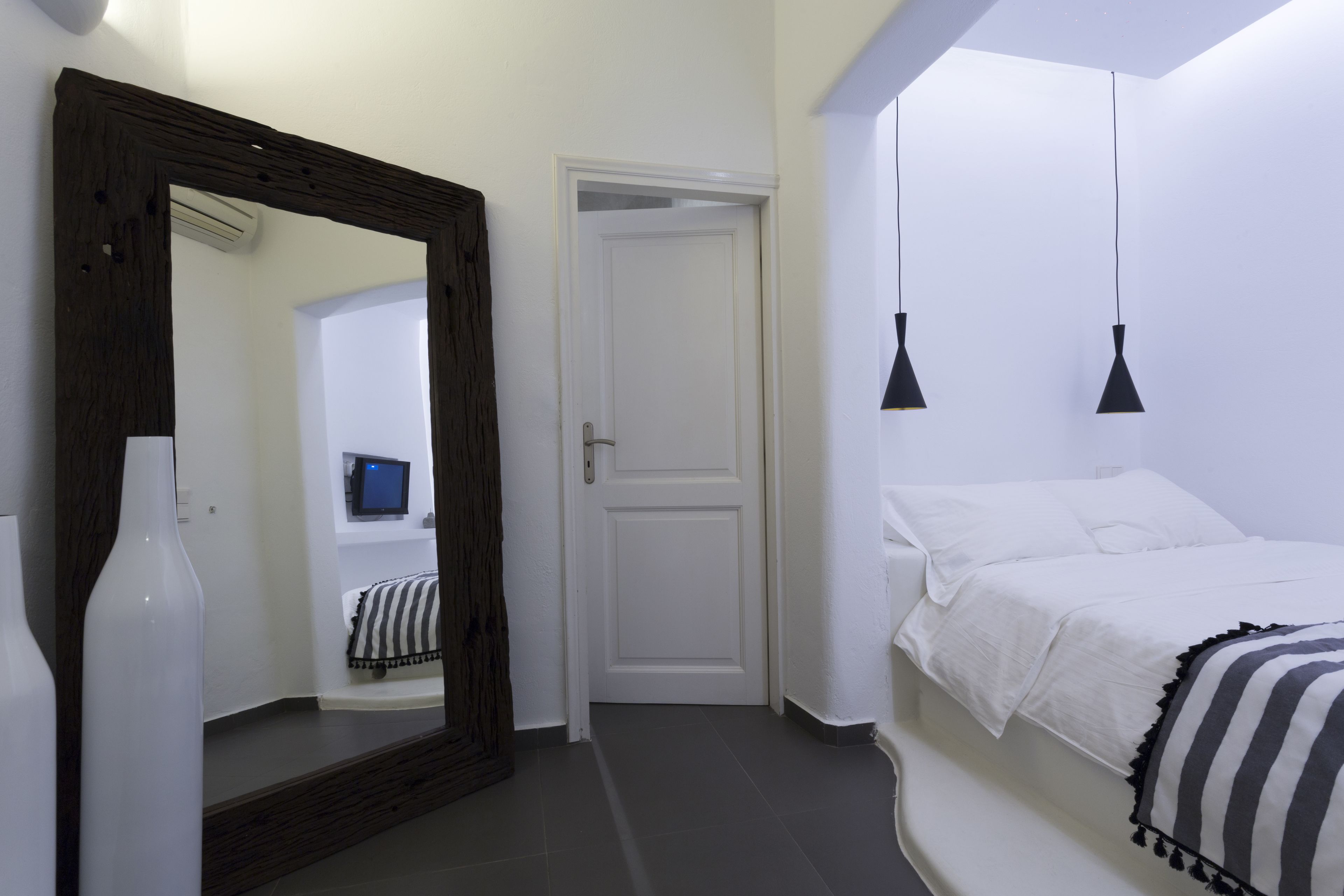 Ein Schlafzimmer mit einem großen Spiegel, einem Bett mit gestreifter Bettwäsche und zwei Pendelleuchten.