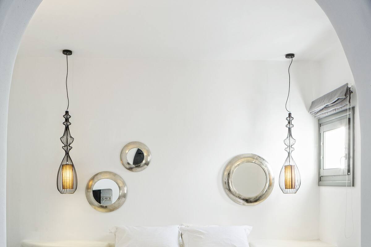 A modern bedroom with a large bed, two bedside tables, a small bedside table, a mirror, and a window.