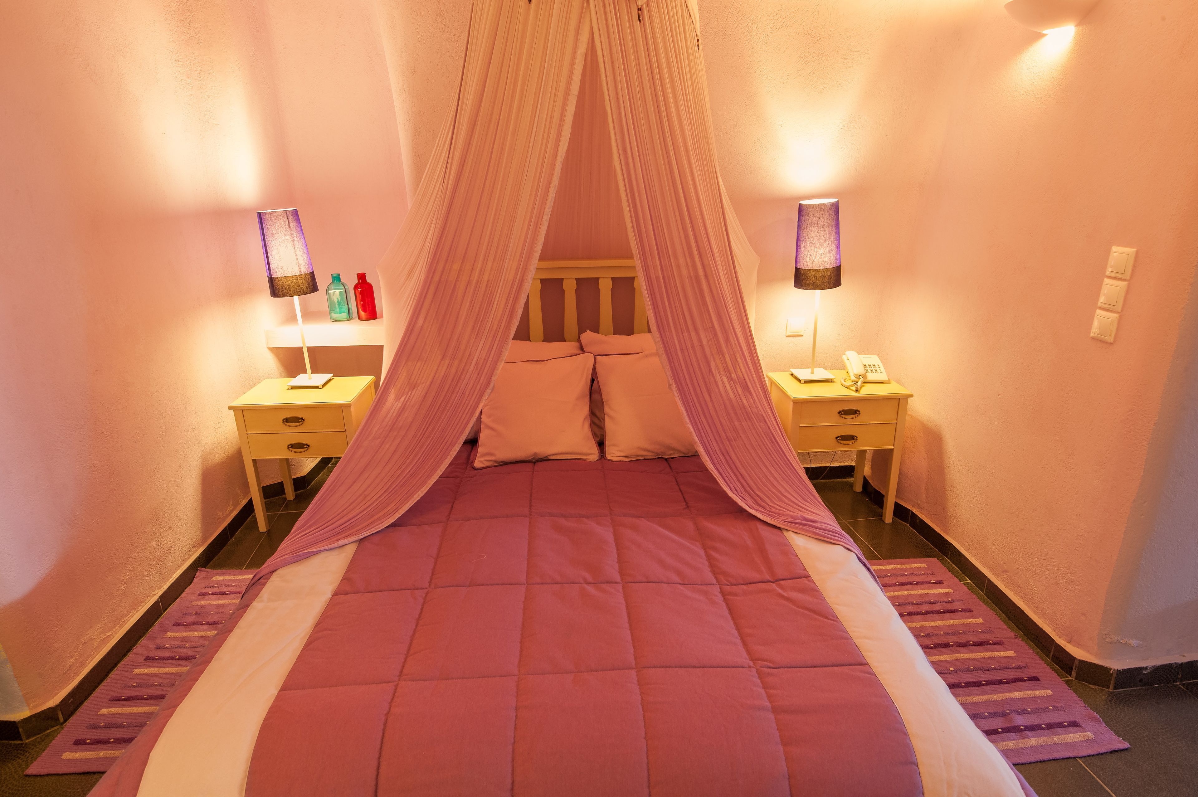 A bedroom with a canopy bed, bedside tables with lamps, and a nightstand with a phone.