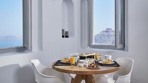 A breakfast table with plates of food, glasses of orange juice, and a view of a mountainous landscape through large windows. - Aroma Suites (Santorini)