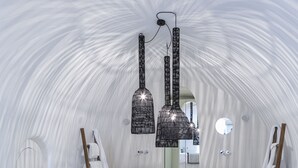 A modern, white-themed spa room with a central hot tub, wooden ladder, and two hanging black chandeliers. - Aroma Suites (Santorini)