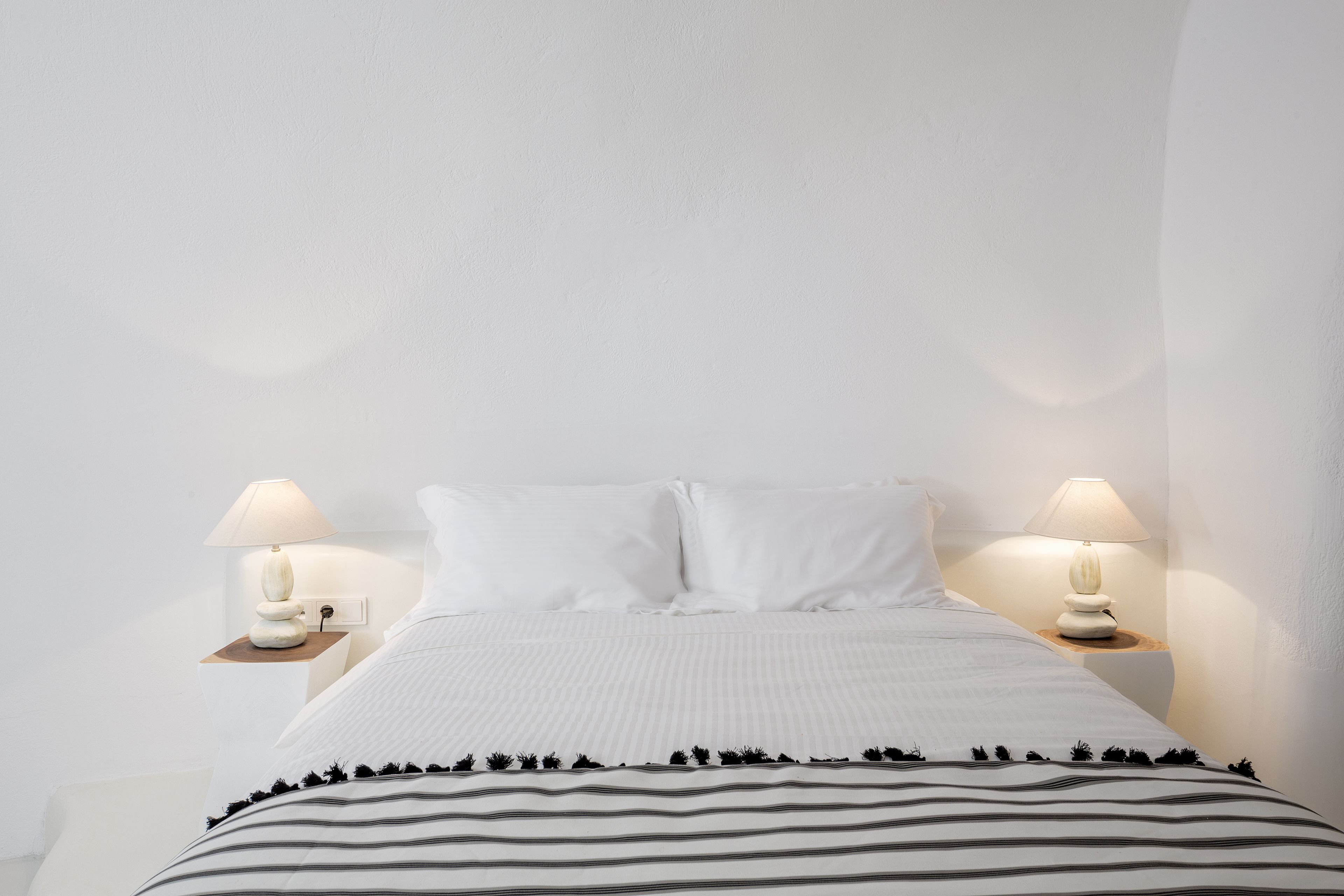 Un lit bien fait, avec une literie blanche et des oreillers à rayures, flanqué de deux tables de chevet sur lesquelles sont posées des lampes.