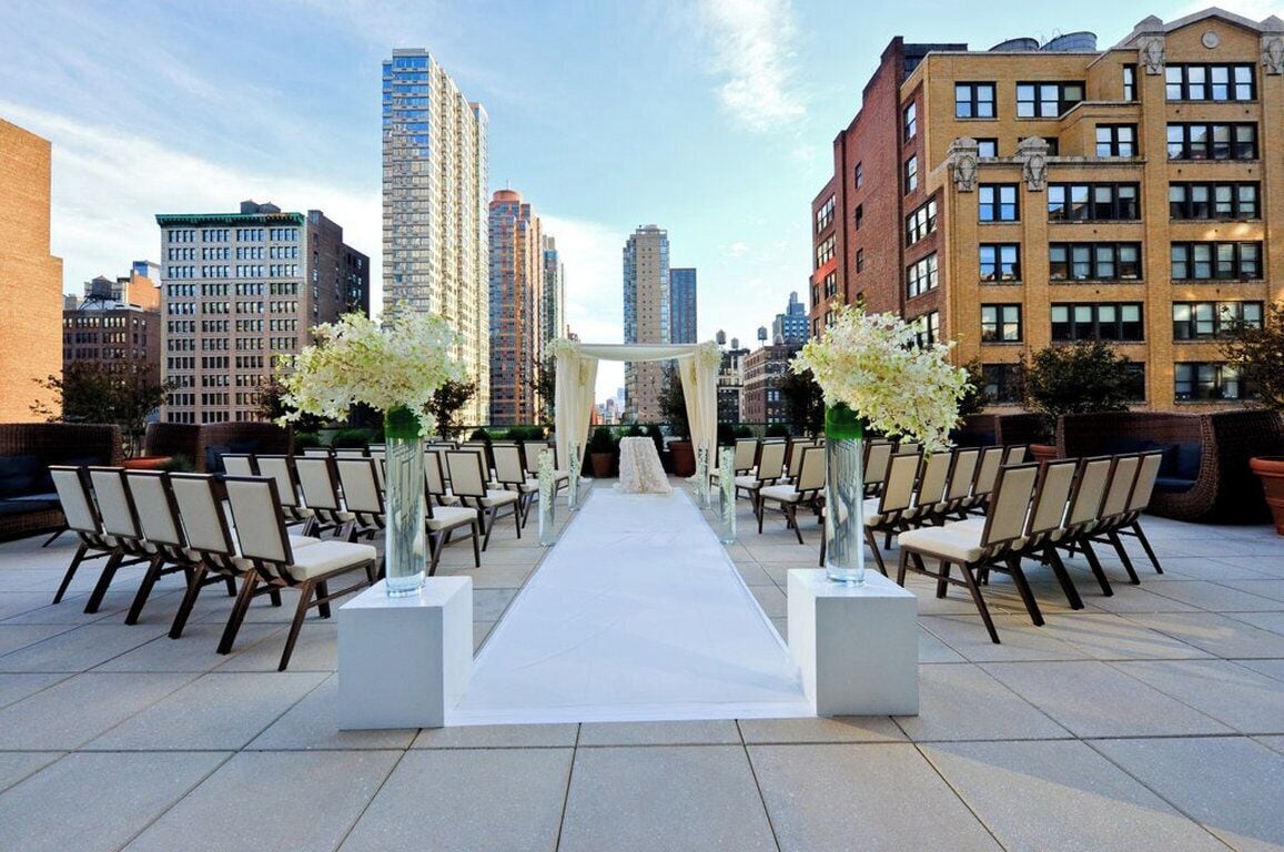 An outdoor wedding ceremony setup with a white aisle, chairs, and floral arrangements.