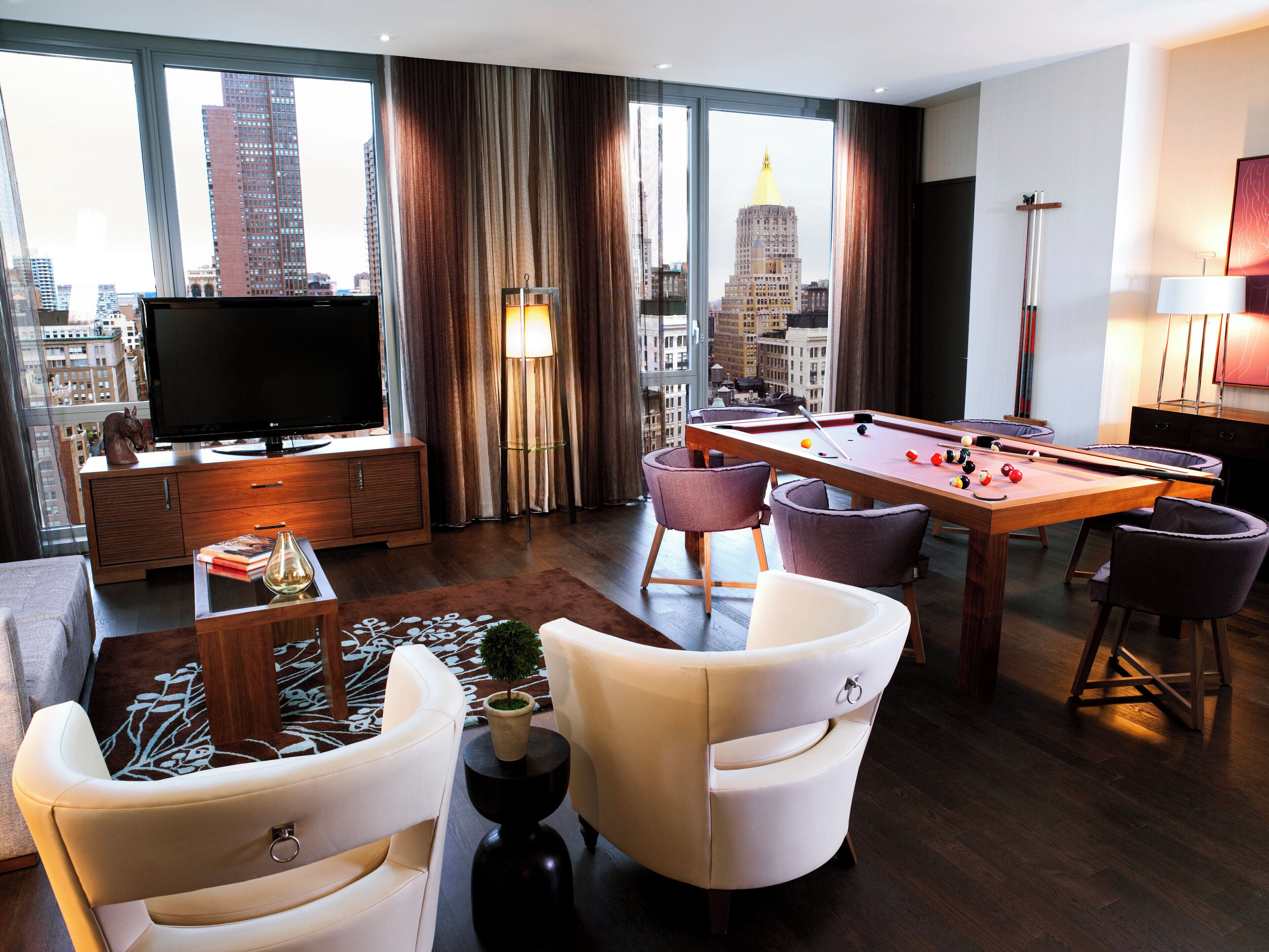 A modern living room with a pool table, comfortable seating, a television, and a city view.