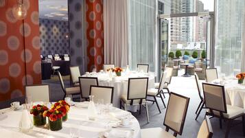 A hotel dining area with round tables set for service, large windows offering city views, and a patterned wall design.