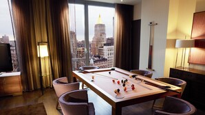 Une table de billard avec des billes, quatre chaises, un téléviseur et une vue sur le paysage urbain à travers de grandes fenêtres.