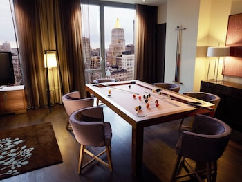 A modern hotel room with a large window, a flat-screen TV mounted on the wall, a sofa, a chair, and a small table with a book and a vase. at Kimpton Hotel Eventi by IHG