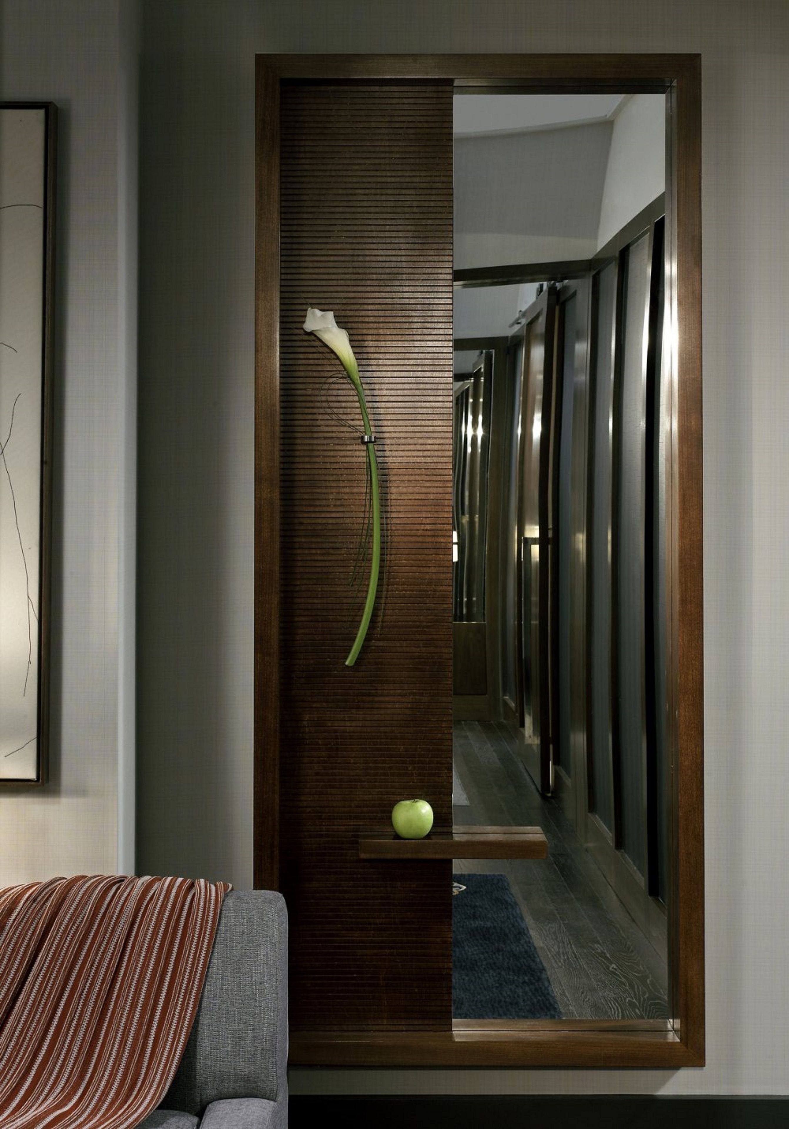 Une pièce moderne avec un mur lambrissé en bois, un miroir qui reflète un couloir et une pomme verte posée sur une étagère.