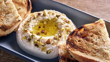 A plate with a creamy white dip garnished with chopped nuts and a drizzle of olive oil, accompanied by toasted bread slices.