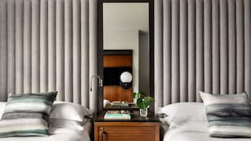 A hotel room with two beds, a wooden nightstand, a mirror, a lamp, and a plant.