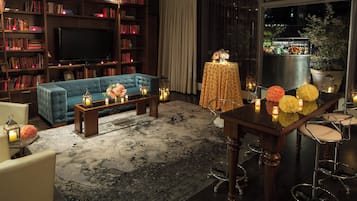 Ein gemütliches Wohnzimmer mit einem blauen Sofa, einem Couchtisch und einer Bar mit Hockern. Ein Bücherregal voller Bücher und ein Flachbildfernseher sind ebenfalls vorhanden.