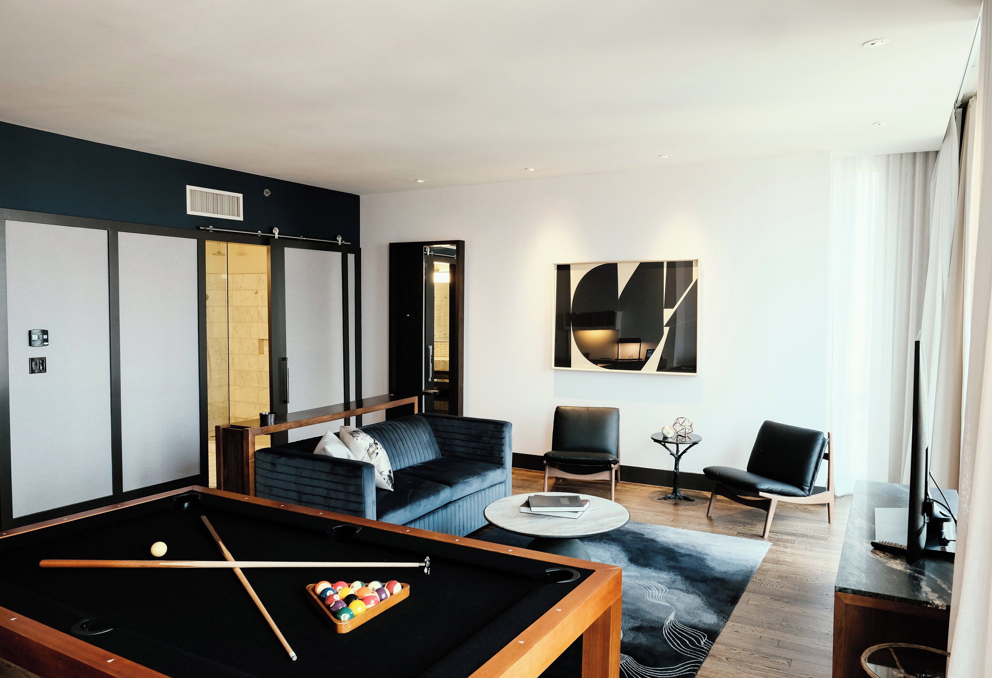 A modern living room with a pool table, a sofa, and two chairs.