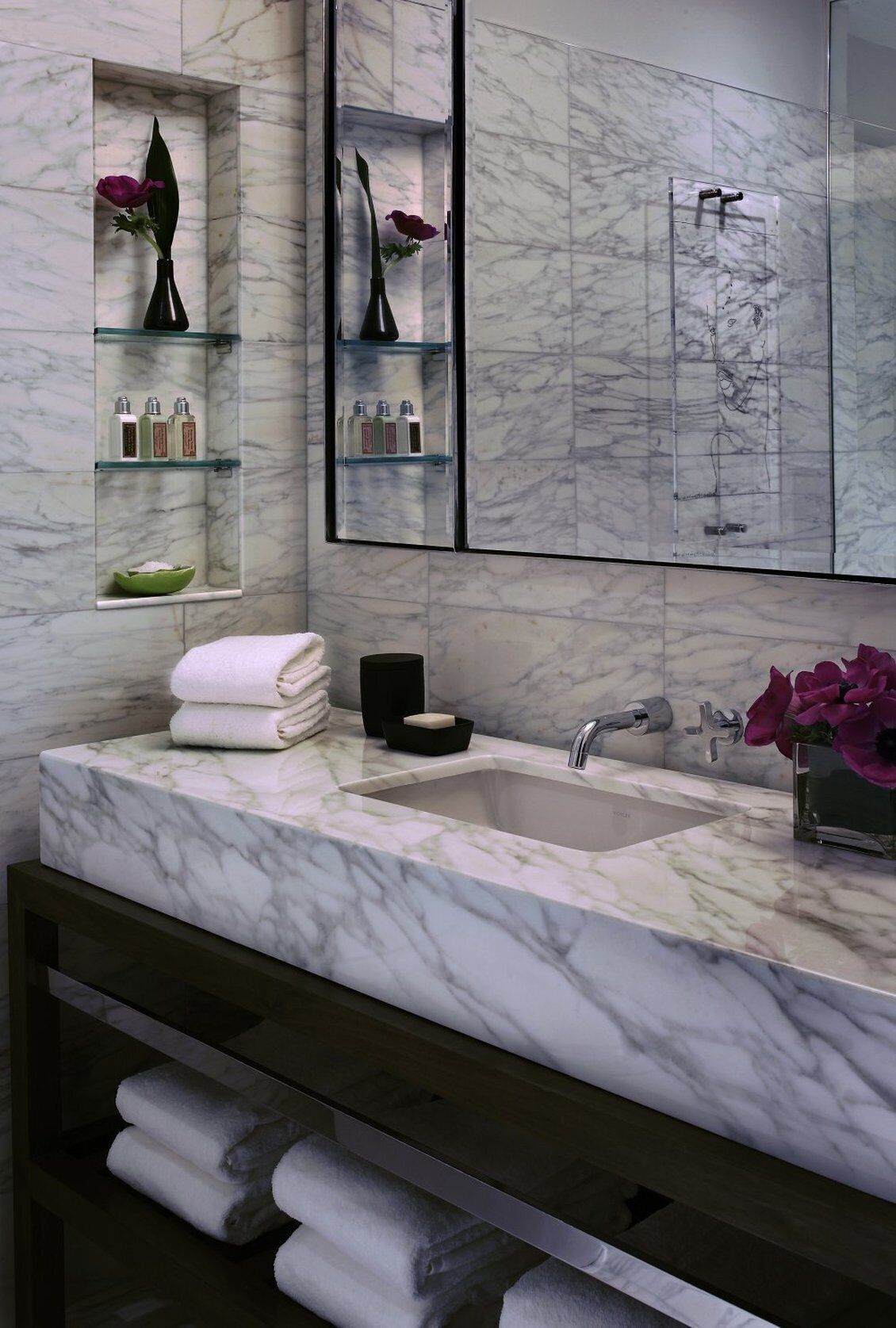A modern bathroom with a marble sink, glass shelves, and a large mirror.
