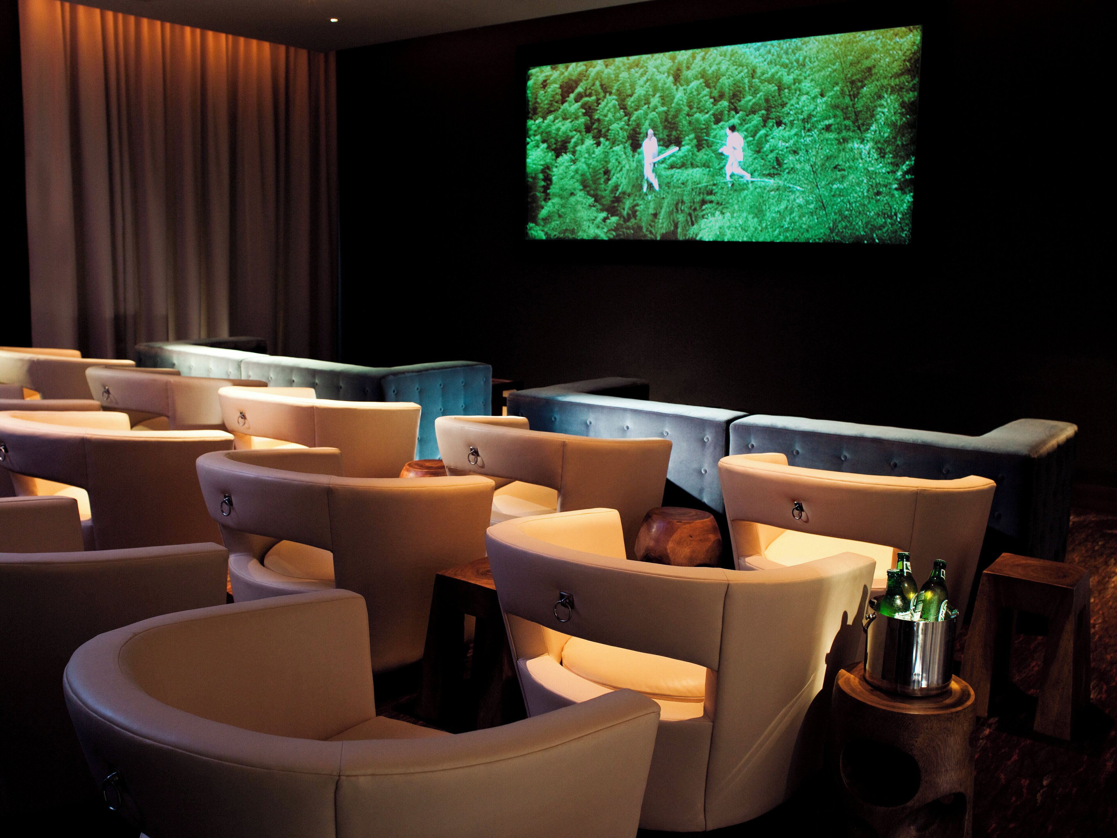 A cinema room with multiple cushioned seating and a screen displaying an outdoor scene.