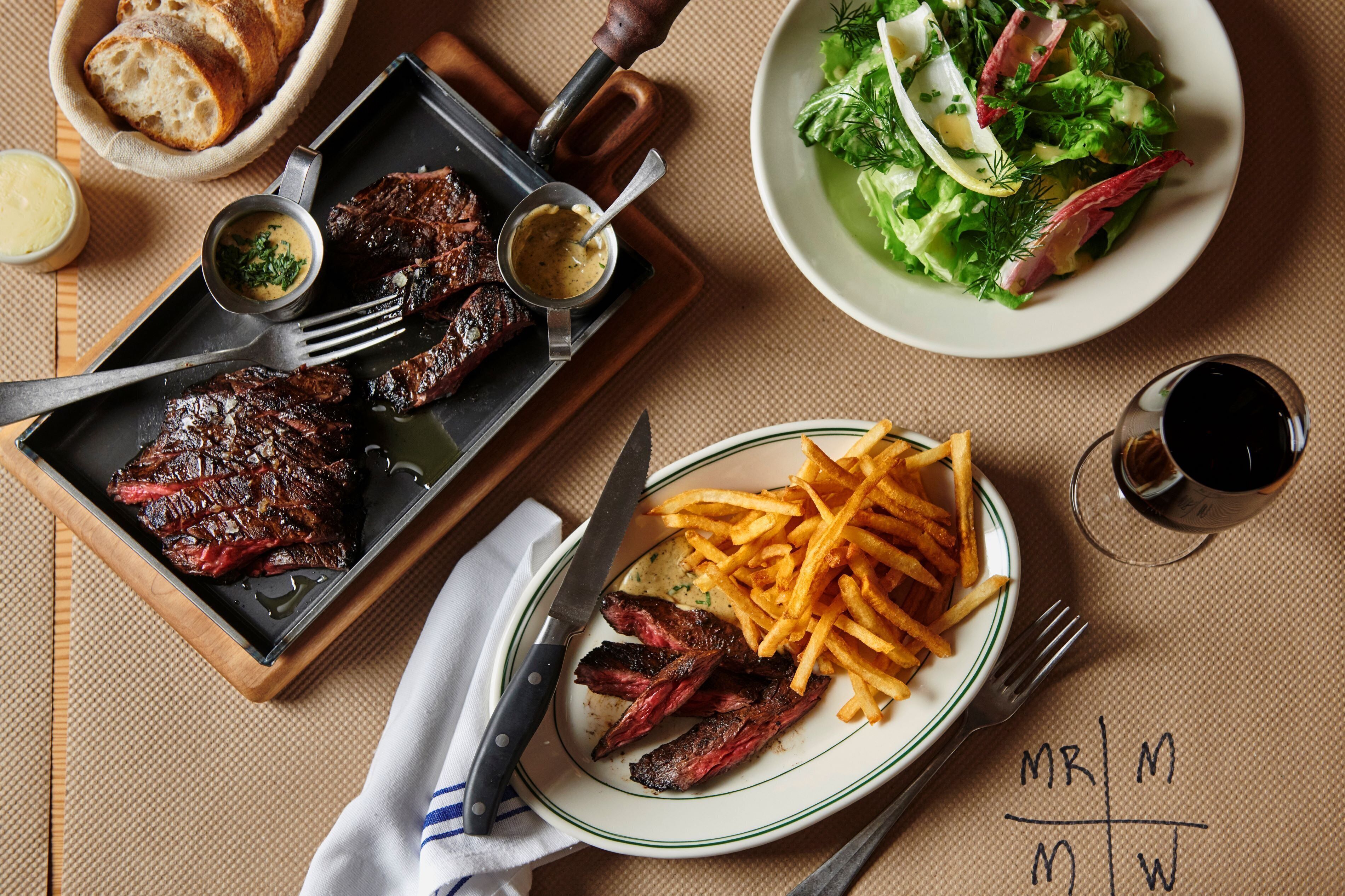 Una mesa de comedor con un bistec, papas fritas y una ensalada.