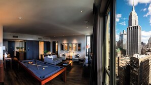 Une chambre d’hôtel moderne équipée d’une table de billard, d’un coin salon et d’une grande fenêtre donnant sur le panorama de la ville.