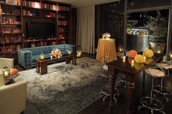 A modern living room with a sofa, armchairs, a coffee table, and a view of a cityscape through large windows. at Kimpton Hotel Eventi by IHG