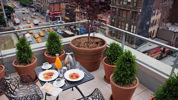 En balkon med et bord dækket til morgenmad, omgivet af krukker med planter, med udsigt over en travl gade.