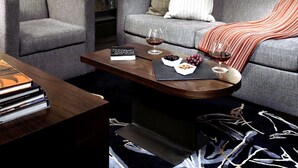 Un salon moderne avec un canapé, des fauteuils, une table basse et une vue sur le paysage urbain grâce à de grandes fenêtres.