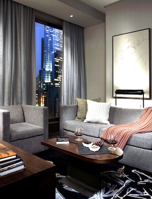 Un salon moderne avec un canapé, des fauteuils, une table basse et une vue sur le paysage urbain grâce à de grandes fenêtres.