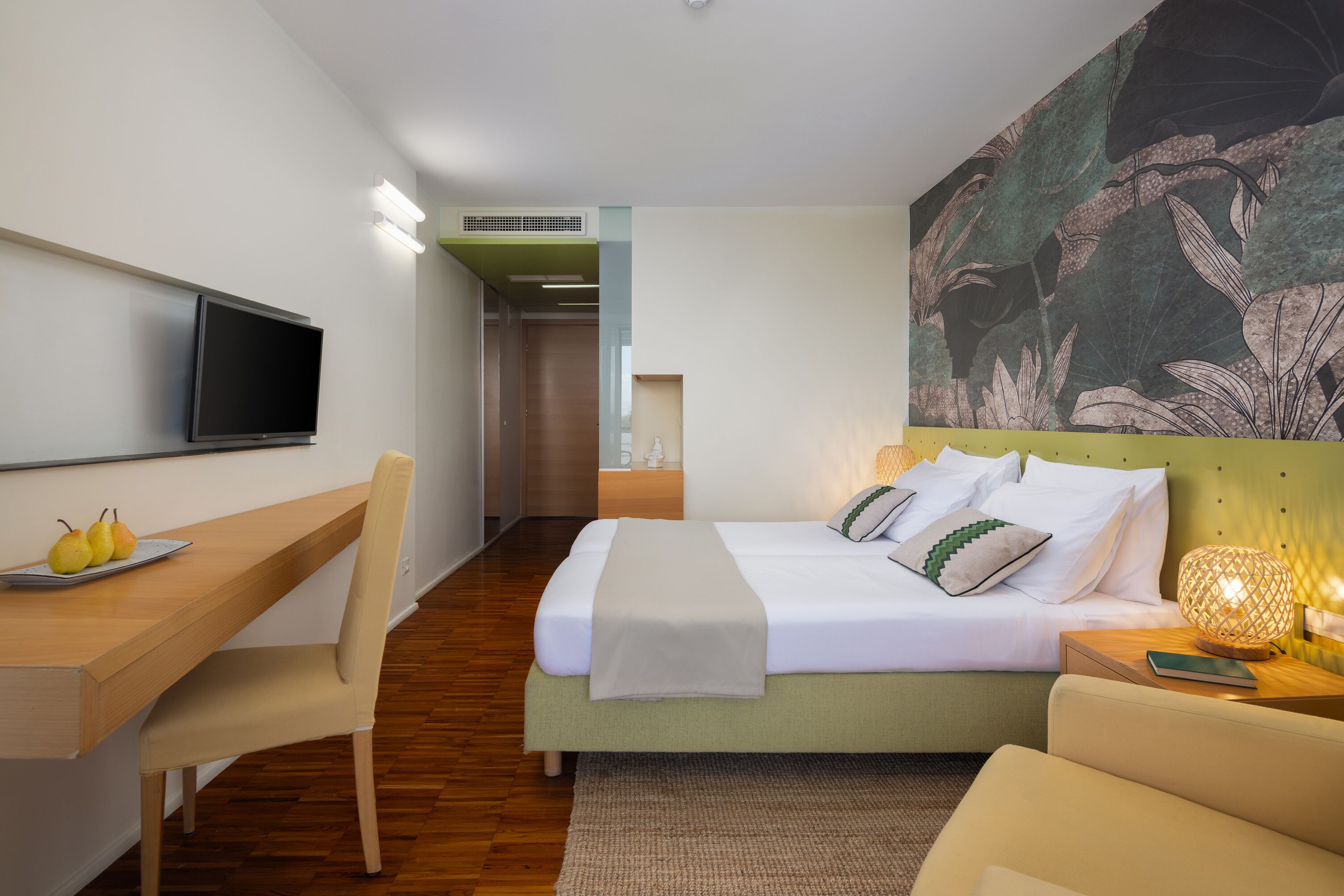 A modern hotel room with a bed, desk, chair, and a television.