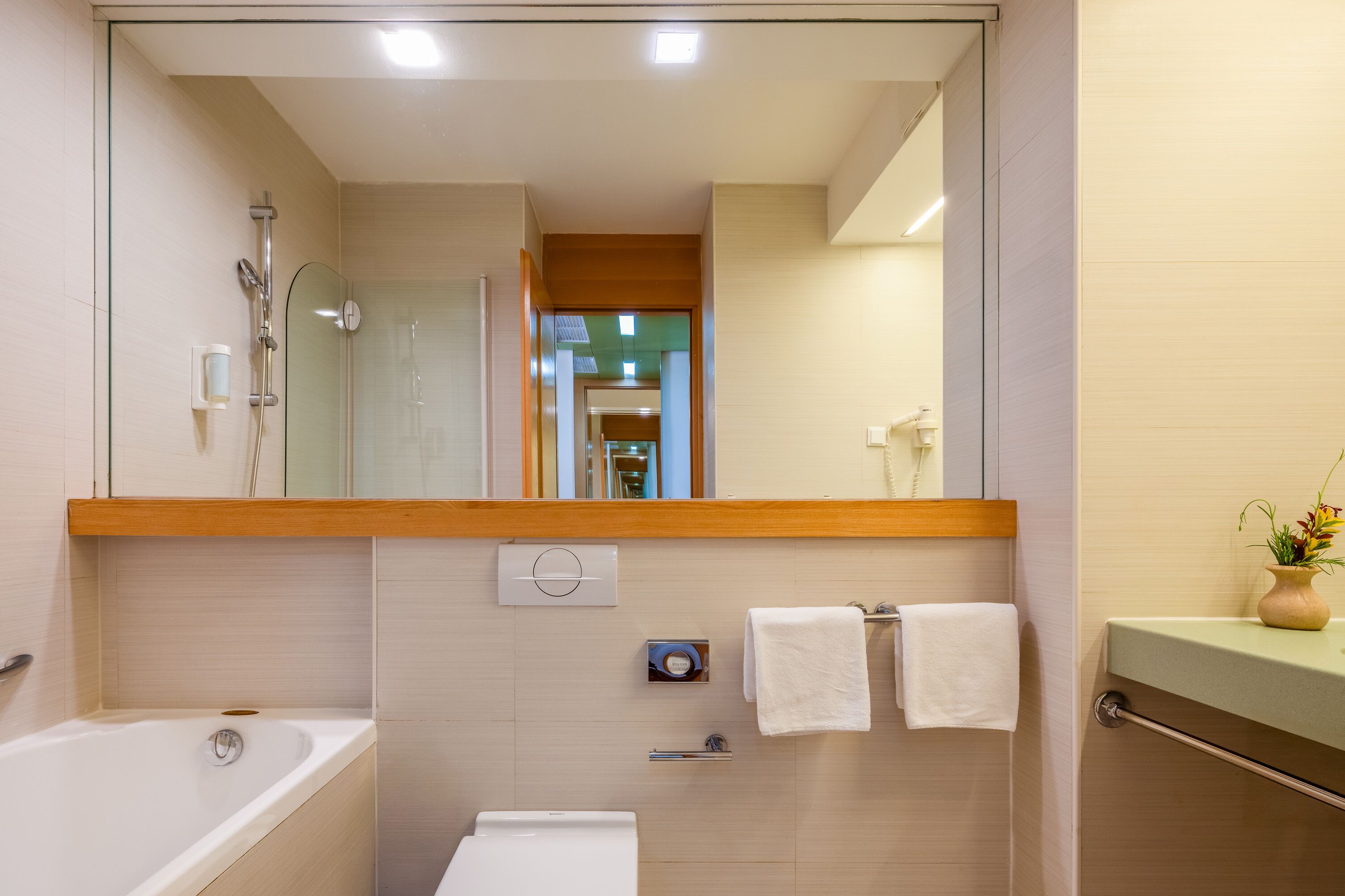 A modern bathroom with a glass shower enclosure, a bathtub, a toilet, and a vanity with a vase of flowers.
