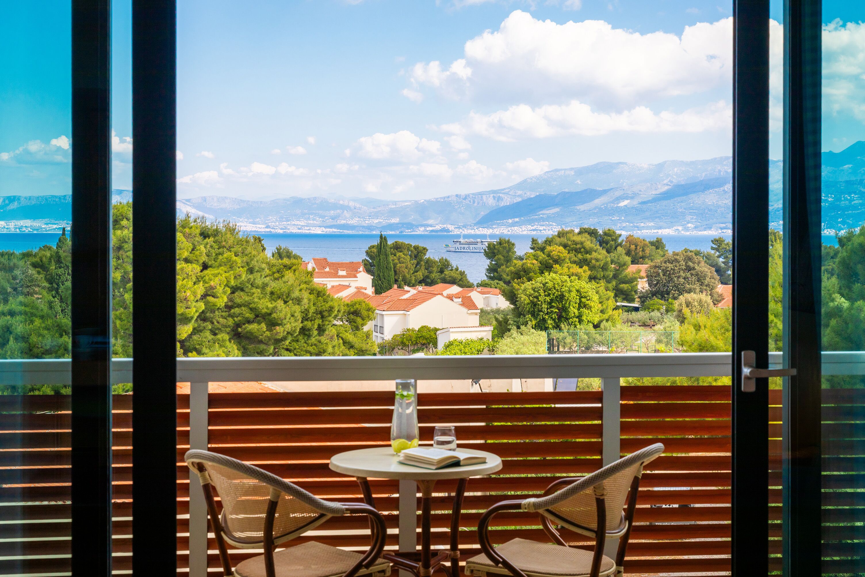 Un balcón con mesa y sillas, con vista panorámica a un lago, montañas y edificios.
