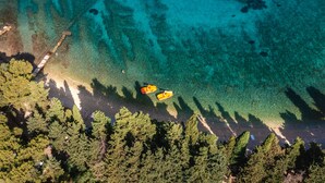 An aerial view of a coastal area with clear turquoise waters, a sandy beach, and dense green forest. - Aminess Vival Velaris Resort  (Supetar)