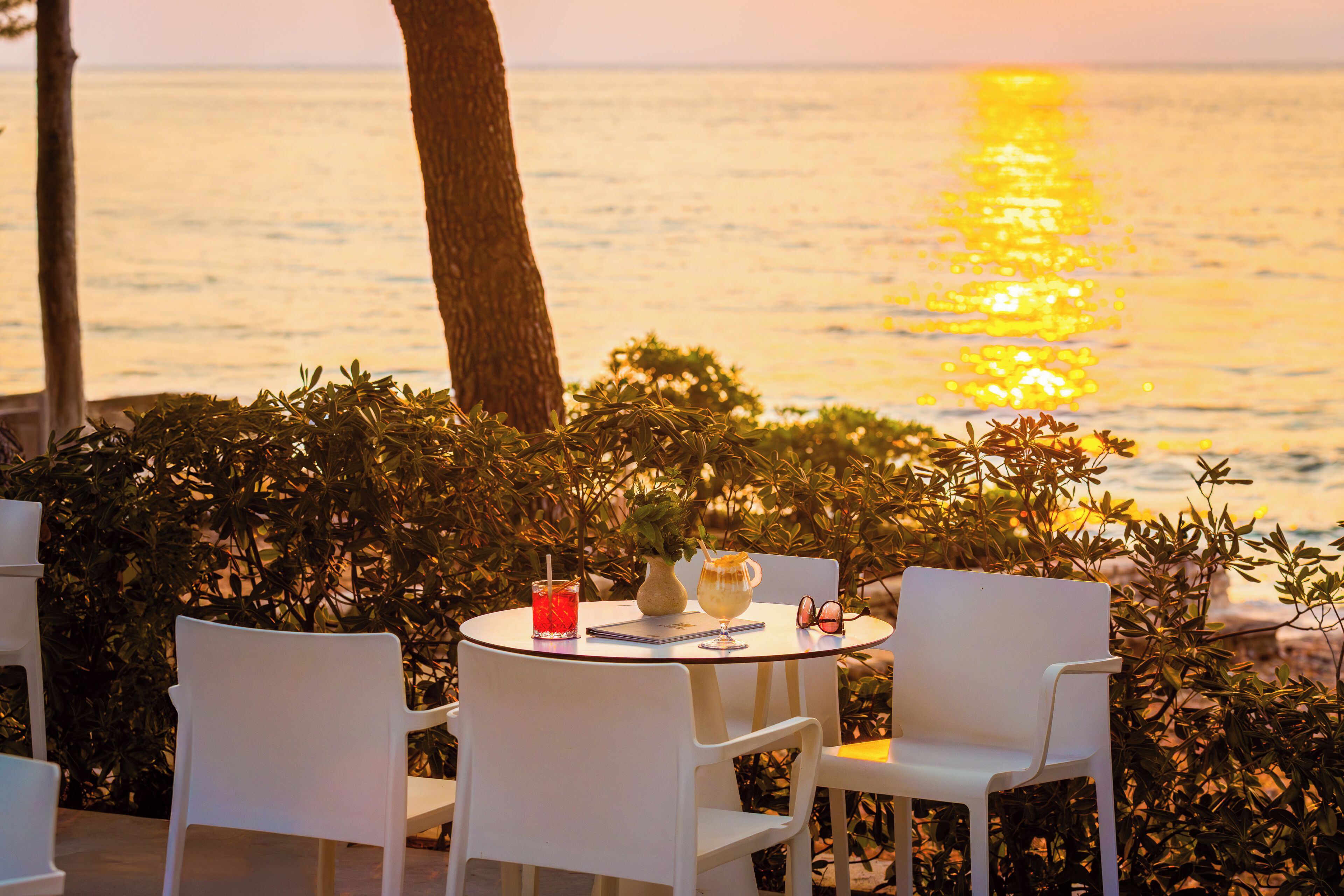 Ein Tisch mit Stühlen und einem Getränk mit Blick auf das Meer bei Sonnenuntergang.