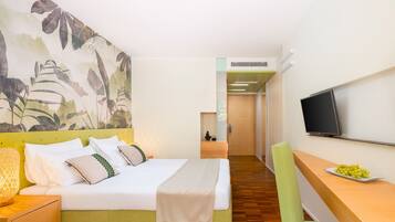 Habitación de hotel con cama, escritorio con televisor, televisor montado en la pared y un mural vegetal en la pared.