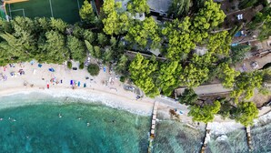 An aerial view of a beach with clear turquoise waters, a sandy shore, and a row of trees. - Aminess Vival Velaris Resort  (Supetar)