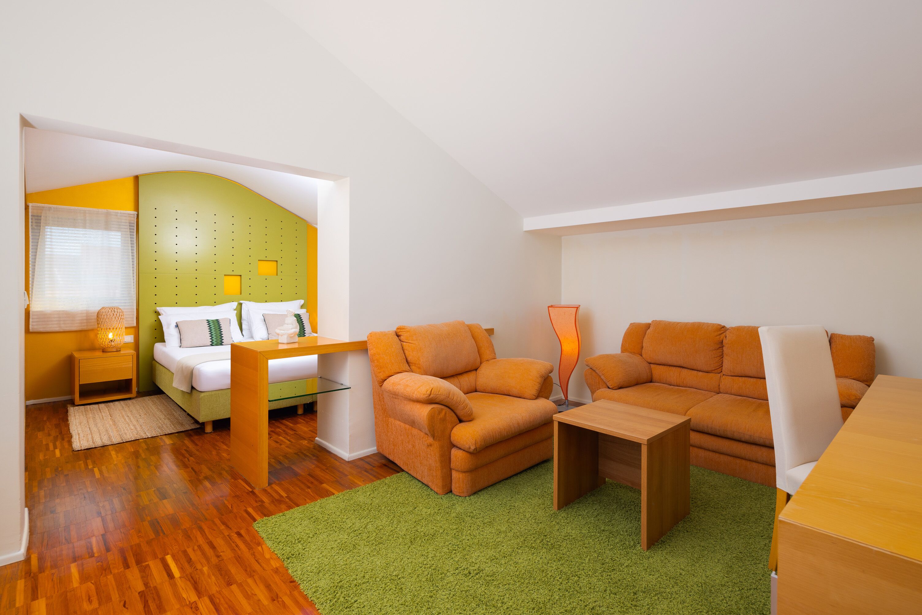 Una habitación moderna y luminosa con una cama, un sofá naranja y una mesa de centro de madera.