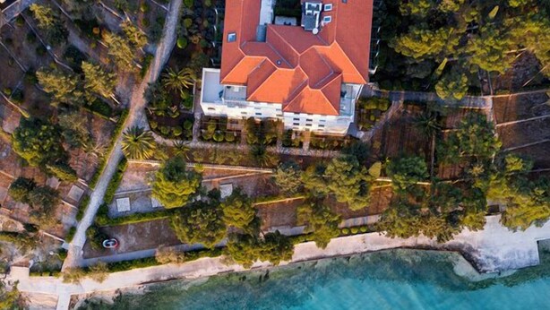 An aerial view of a house with a red roof, surrounded by a clear blue sea and lush greenery. - Aminess Vival Velaris Resort  (Supetar)