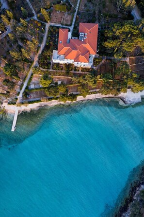 Vista aérea de una casa con techo rojo, rodeada de un mar azul cristalino y abundante vegetación.